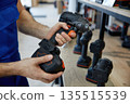 A man is holding a black and orange handheld drill in both hands 135515539