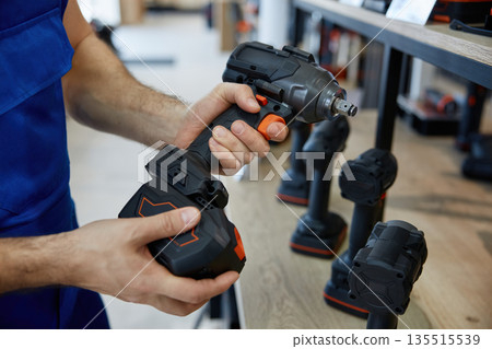 A man is holding a black and orange handheld drill in both hands A man is holding a black and orange handheld drill in both hands 135515539