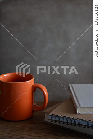 Orange cup with notes on table. Stack of notepads with a tea cup on beige background. Writing pads and mug. Writer interior. Cozy home. Orange cup with notes on table. Stack of notepads with a tea cup on beige background. Writing pads and mug. Writer interior. Cozy home. 135516124