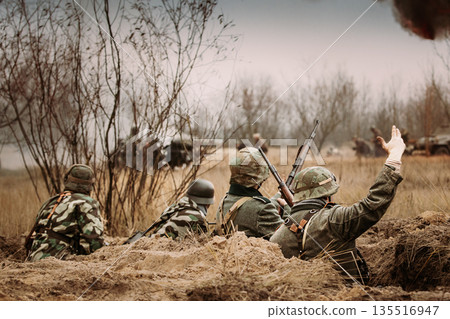 Defensive Position. Re-enactors Armed Rifles And Dressed As World War Ii German Wehrmacht Infantry Soldiers Fighting Defensively In Trench. Building On Fire On Background 135516947