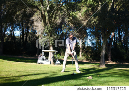 Male golfer in action during game on golf course under sunlight. Male golfer in action during game on golf course under sunlight. 135517725