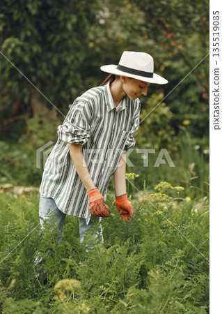 Young woman taking care of plants. Brunette in a hat and gloves. 135519085