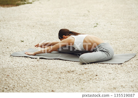 Pretty lady training on a summer beach. Brunette doing yoga. Girl in a sportsuit. 135519087
