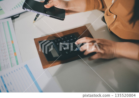 Business woman using calculator to calculate financial report, working at office with laptop computer on table. Asian female accountant or banker making calculations. finances and economy concept Business woman using calculator to calculate financial report, working at office with laptop computer on table. Asian female accountant or banker making calculations. finances and economy concept 135520804