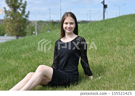 Woman in black dress sitting on green grass, smiling on a sunny day outdoors. Woman in black dress sitting on green grass, smiling on a sunny day outdoors. 135521425