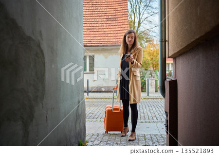 Woman traveler with suitcase using smartphone in narrow city street Woman traveler with suitcase using smartphone in narrow city street 135521893