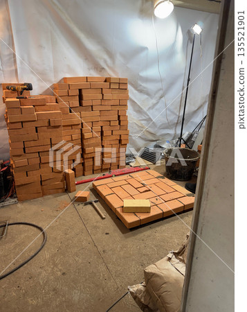 A stove base laid out of brick. A stack of bricks and tools nearby. Construction of a new heating stove. A stove base laid out of brick. A stack of bricks and tools nearby. Construction of a new heating stove. 135521901