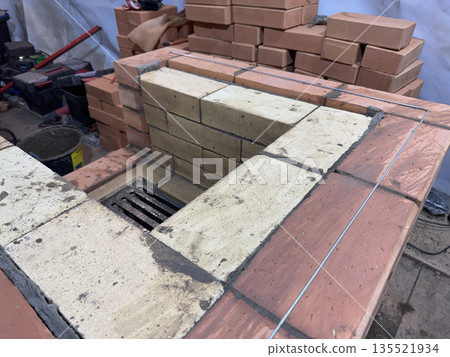 Fresh brickwork of a heating stove. The firebox is made of fireclay brick. The masonry is reinforced with wire. Oblique Angle. Fresh brickwork of a heating stove. The firebox is made of fireclay brick. The masonry is reinforced with wire. Oblique Angle. 135521934
