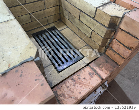 Fresh brickwork of a heating stove. The firebox is made of fireclay brick, a cast iron grate is installed. Close-up. 135521939
