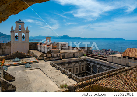 Panoramic top view of Naples rooftops from Castel Sant Elmo, with the sea in the distance and Mount Vesuvius rising above the city on a clear summer day. 135522091