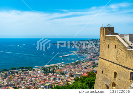 Panoramic top view of Naples rooftops from Castel Sant Elmo, with the sea in the distance and Mount Vesuvius rising above the city on a clear summer day. 135522096
