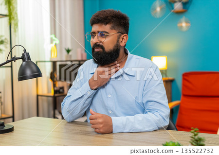 Indian man clutching throat painful swallow virus infection sharp pain feels seriously sick indoors 135522732