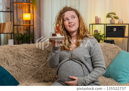Pregnant woman making birthday wish blowing out cake candle celebrating special home moment Pregnant woman making birthday wish blowing out cake candle celebrating special home moment 135522737