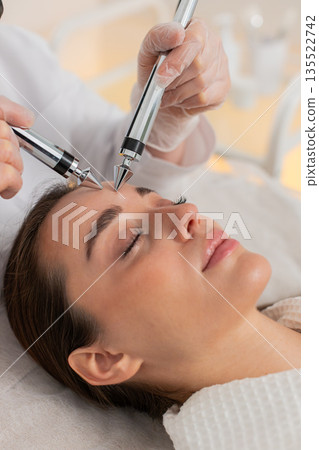 Beautician doctor makes woman micro currents face therapy using electrical impulses in spa salon Beautician doctor makes woman micro currents face therapy using electrical impulses in spa salon 135522742