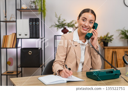 Young businesswoman answers retro landline from nineties speaks clear business talk and writes notes 135522751