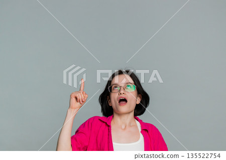 Young woman smiles suddenly raises finger up after thinking moment showing eureka idea inspiration Young woman smiles suddenly raises finger up after thinking moment showing eureka idea inspiration 135522754