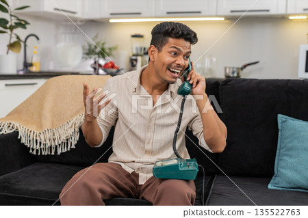Indian man talks on retro corded phone nostalgic call listens and speaks with smile and gentle laugh Indian man talks on retro corded phone nostalgic call listens and speaks with smile and gentle laugh 135522763