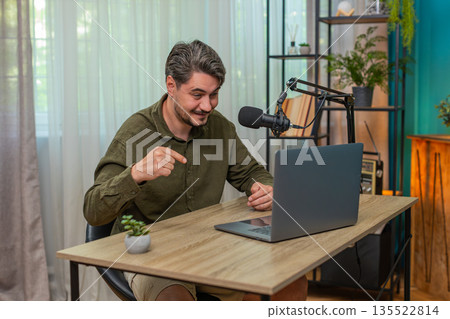Middle-aged man hosting live vlog speaking to laptop microphone engaging interaction at table desk 135522814