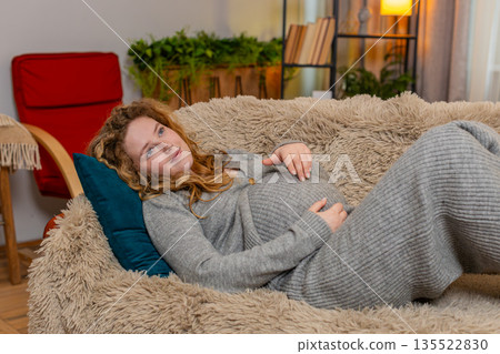 Pregnant woman lying on home sofa, gently touching belly with hands calm and relaxed peaceful moment 135522830