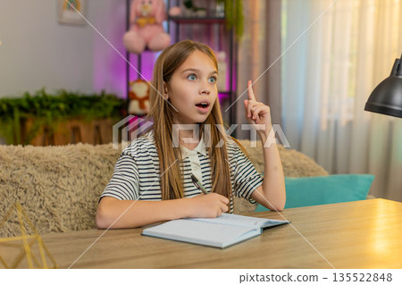 Child girl kid doing school homework at table happily solving problem excited expression at home Child girl kid doing school homework at table happily solving problem excited expression at home 135522848