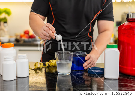 Sportsman pours supplement powder into glass of water in kitchen at home for daily fitness energy up 135522849