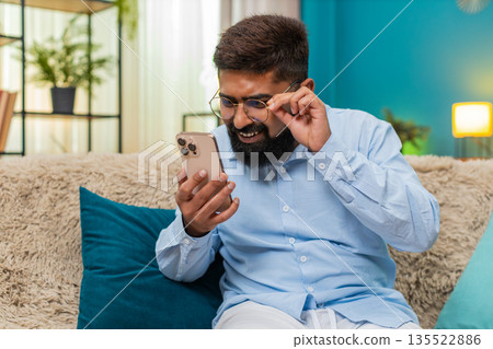 Indian man in glasses squints to read tiny smartphone text brings screen close showing concentration Indian man in glasses squints to read tiny smartphone text brings screen close showing concentration 135522886