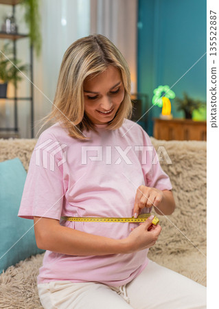 Pregnant woman measuring belly with tape smiling satisfied with progress expecting baby birth soon Pregnant woman measuring belly with tape smiling satisfied with progress expecting baby birth soon 135522887