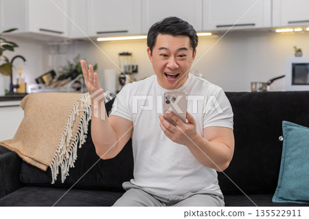 Asian man celebrates app win with smartphone shares good news via social media chat smiling excited 135522911