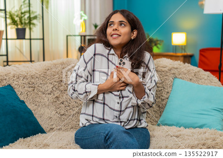 Indian woman reads smartphone message smiles holds phone to chest moved by touching text feeling joy 135522917
