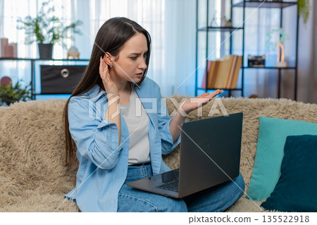 Young woman irritated sits on sofa arguing over laptop poor video call emotionally gesturing angry 135522918