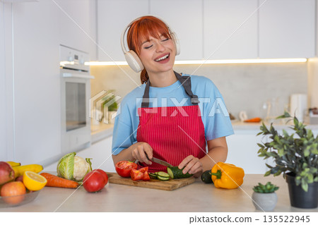 Young woman slices cucumber tomato on cutting board makes colorful salad and tastes fresh bite smile Young woman slices cucumber tomato on cutting board makes colorful salad and tastes fresh bite smile 135522945