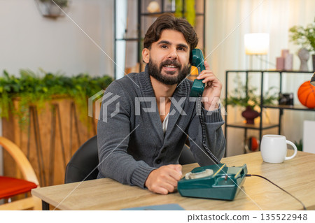 Indian man talks on retro wired telephone from nineties smiles places handset back on base with care Indian man talks on retro wired telephone from nineties smiles places handset back on base with care 135522948