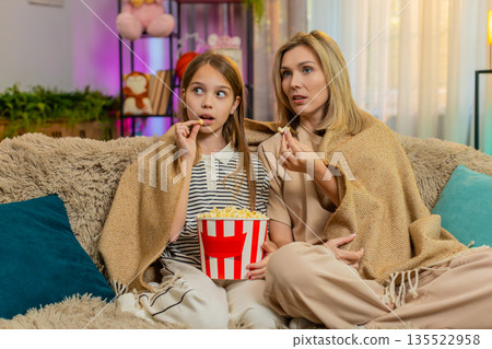 Child girl kid with mother watching cartoon together at home on sofa under warm blanket in room 135522958