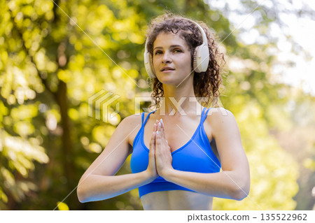Woman sitting on mat in lotus position, relaxing practicing yoga meditation in park on summer day Woman sitting on mat in lotus position, relaxing practicing yoga meditation in park on summer day 135522962