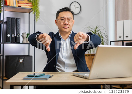 Upset businessman showing thumbs down, dislike bad work, disapproval dissatisfied feedback at office Upset businessman showing thumbs down, dislike bad work, disapproval dissatisfied feedback at office 135523379