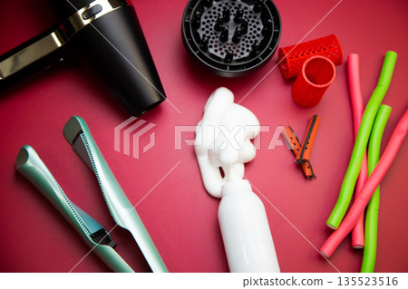 Top view on a pink background, a hairdryer with attachments, stylers and curling irons for straightening and creating curls, foam for creating volume and long-term holding, curlers of different shapes 135523516