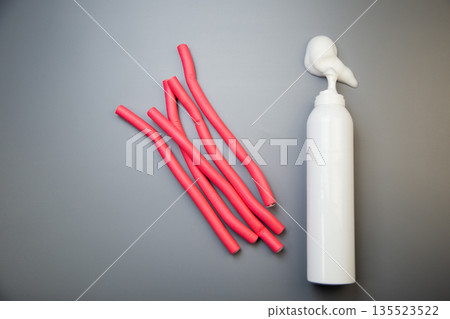 On the side, on a gray background, there is a bottle of foam for long-term hair styling, white foam poured out of it, pink bendable curlers with space for text lie nearby. The concept of styling 135523522