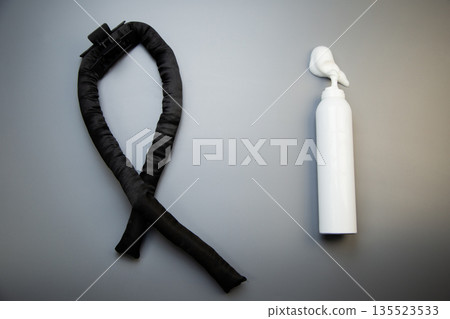 Close-up of hair styling foam in a white bottle, next to it curlers to create root hair volumes on a gray background with space for text. The concept of long-term hair styling, hairstyles, curls and 135523533