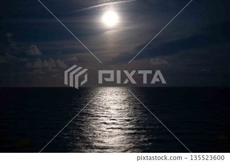 Mystical full moon over tranquil ocean with shimmering reflection and wispy clouds 135523600