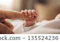 Small hand holds adult finger in a warm indoor setting during a quiet moment of connection between a parent and baby 135524236