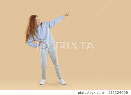 Cheerful young woman pointing with finger to place for advertising text or logo of your store. 135524666
