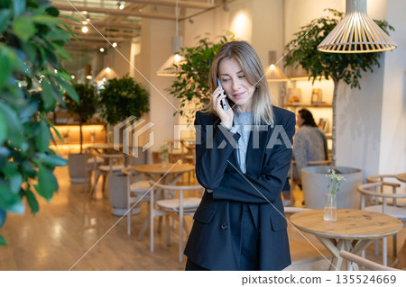 Smiling relaxed businesswoman restaurant business owner chatting on smartphone with colleagues. 135524669