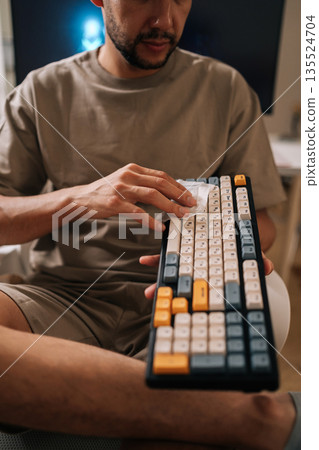 Vertical cropped shot of technician cleaning mechanical keyboard, wiping dust and germs from input device keys. Maintaining hygiene and sanitation for computer equipment at home or office workspace. 135524704