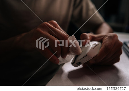 Man cleaning computer mouse with disposable wipe, emphasizing hygiene and sanitation for workspace and technology during daily routines at home or office. Concept of service, cleaning PC. 135524727