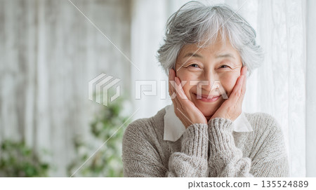 一位老人在窗邊擺姿勢，用手托著臉頰微笑 135524889