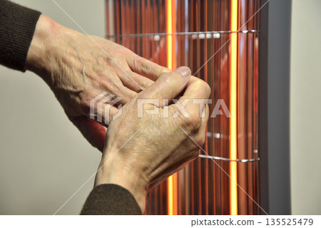 An elderly man's hands warming themselves by an electric heater An elderly man's hands warming themselves by an electric heater 135525479