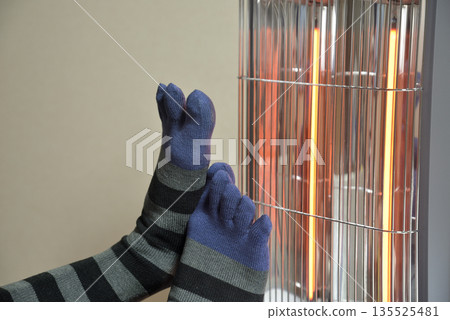 一位老人的雙腳被電暖器溫暖著。 一位老人的雙腳被電暖器溫暖著。 135525481