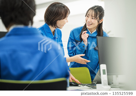 一位身著職業裝的年輕女子正在辦公室與同事交談。 135525599