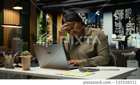 African american woman realizing she works alone late at night in the office, pushing limits despite clear signs of fatigue and tension. Workplace challenges and discouragement. Camera A. African american woman realizing she works alone late at night in the office, pushing limits despite clear signs of fatigue and tension. Workplace challenges and discouragement. Camera A. 135526311