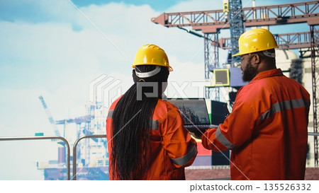 Drilling rig boat engineering team using laptop to monitor equipment systems. Offshore platform teamworking colleagues calibrating gear with notebook program, doing maintenance, 135526332